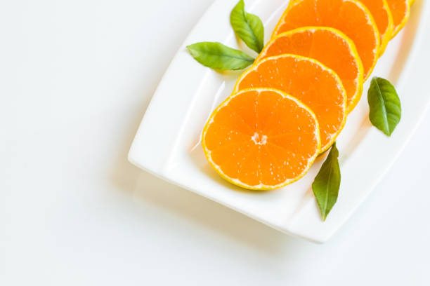 Fresh, natural round sliced tangerine with fresh green leaves designed on a white plate