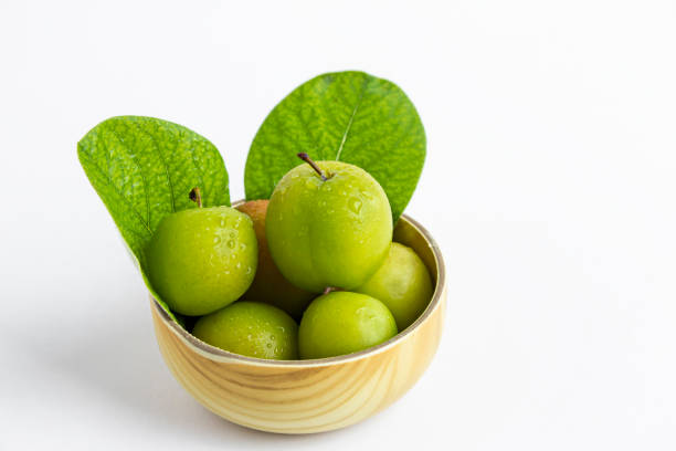 Fresh,green plums in the bamboo bowl with green leaves and water drops on white surface with copy space