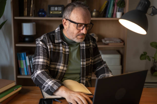 istock Concentrated mature man working at home using laptop and taking notes in his notebook 2206276430