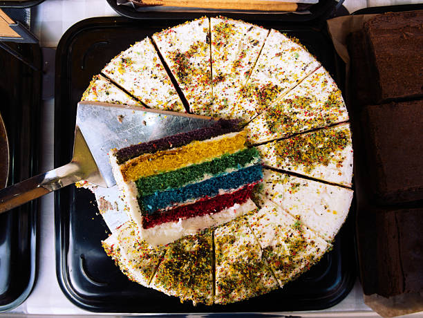 A rainbow cake topped with cream on display at a market
