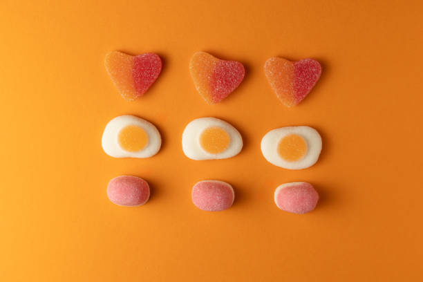 Colorful gummy candies arranged on orange background: hearts, fried eggs, and pink jelly beans