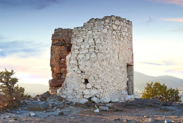Historic stone windmills situated in Turkey amidst a serene mountainous background. The charming rustic architecture testifies to the region's cultural heritage, bathed in the golden hues of early morning sunlight. Close to the city of Bodrum.