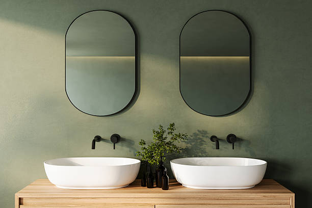 istock A sleek and modern bathroom vanity with dual oval mirrors, white vessel sinks, and black faucets, set against a muted green wall and wooden countertop. Enhanced with greenery for a calm, 3D Rendering 2206281495