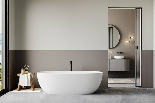 istock Luxury bathroom with a freestanding white bathtub, black faucet, wooden spa stool, and a connected vanity area with a round mirror. Modern minimalist design with natural light. 3D rendering 2206281663