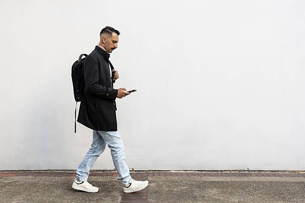 istock Businessman with backpack is on his phone while walking against white wall 2206287137