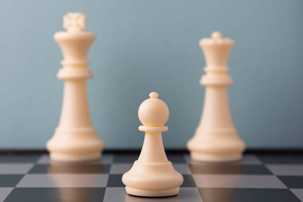 White pawn standing between king and queen on chessboard with blue background, representing strategy and leadership