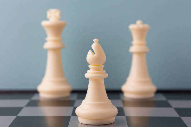 White bishop standing in front of king and queen on chessboard