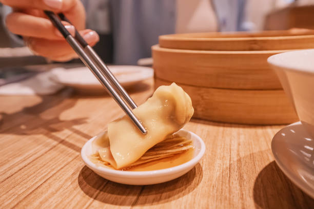 istock Woman using chopsticks dipping wonton dumpling into soy sauce 2206304502