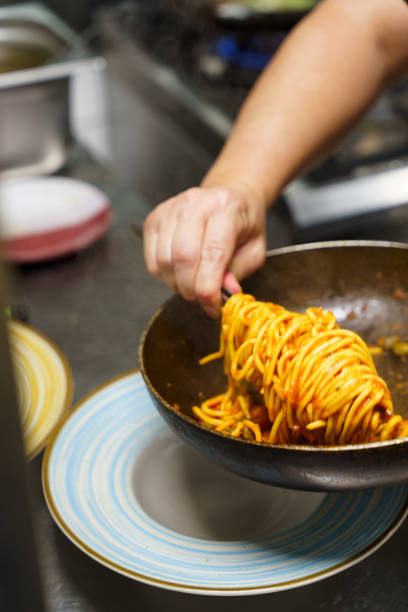 Chef plating spaghetti with tomato sauce in a professional kitchen