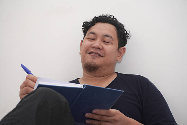 istock Asian man writing daily journal on his diary on bed before sleep, reflecting his life 2206310546