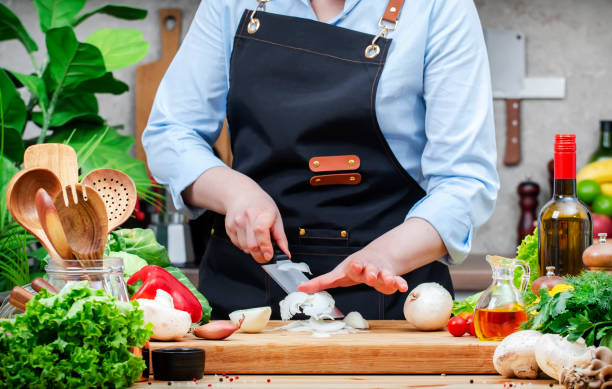 istock Chef moves chopped onion off knife. Cozy kitchen with wooden table, kitchenware, vegetables, herbs and ingredients for cooking. Healthy vegan food, culinary, recipes, blogging 2206325763