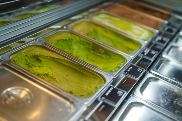 Close-up of matcha and hojicha flavored ice cream stored in stainless steel containers at a modern dessert shop freezer display.