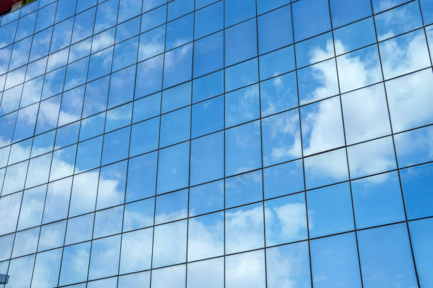 Modern glass building exterior reflecting the blue sky and white clouds in symmetrical window panels.