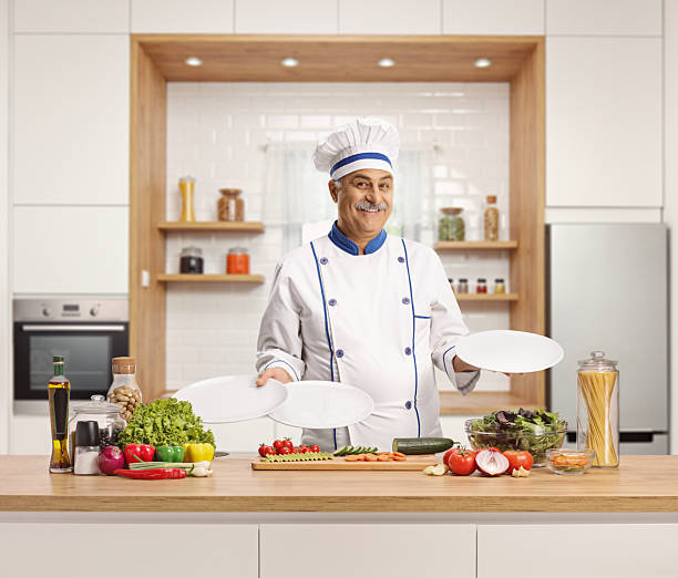 Cheerful mature chef smiling and holding empty plates in a kitchen