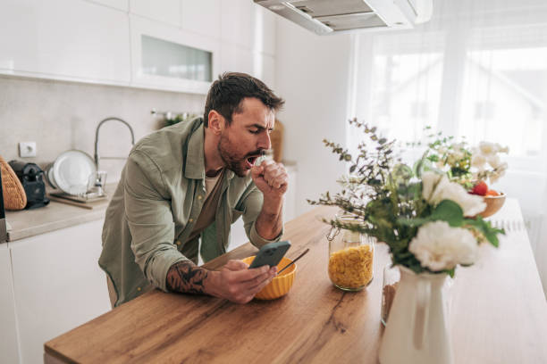 istock Sick man coughing and holding smartphone in kitchen 2206339092