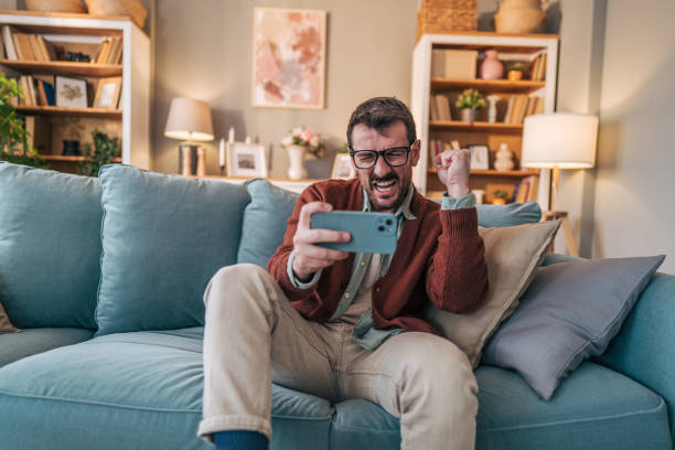 istock Excited man winning mobile game on smartphone at home 2206339358