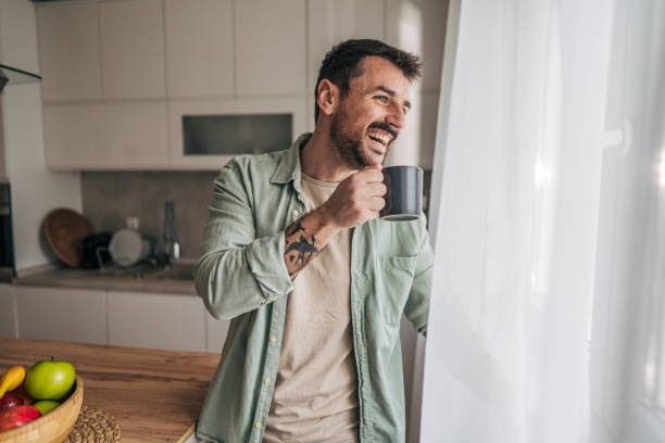 istock Smiling man drinking coffee and looking out the window in his kitchen 2206339744