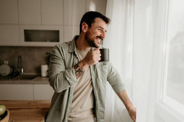 istock Smiling man drinking coffee and looking out the window in kitchen 2206339746