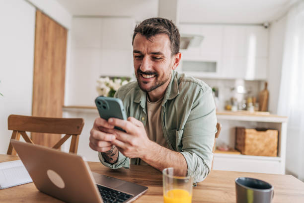 istock Happy freelancer smiling and using smartphone at home in his kitchen 2206339964