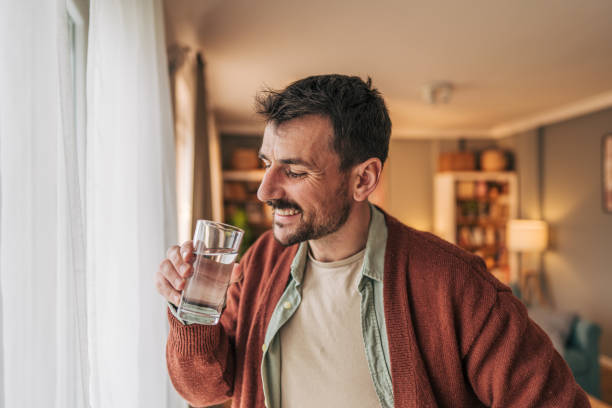 istock Smiling man drinking fresh water by the window at home 2206340158