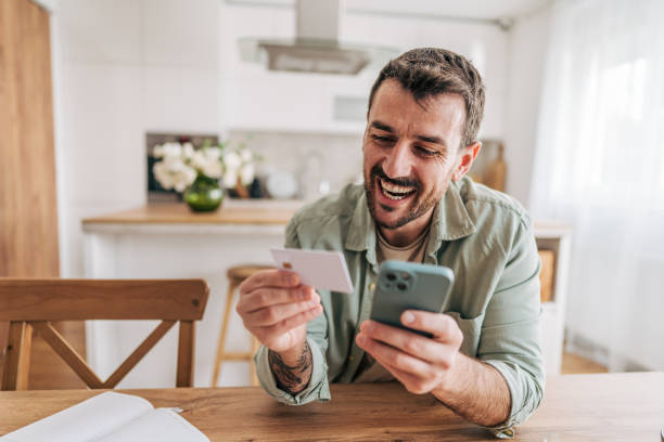 istock Happy man making online payment using credit card and smartphone at home 2206340204