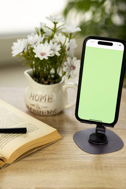 istock A mobile phone with green screen. Smartphone on stand.Book with magnifying glass 2206341789