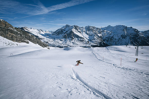 Distant view of snowboarder descending mountain at ski resort, snowcapped mountains in distance, Swiss Alps