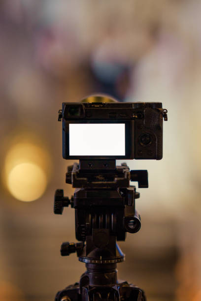 istock Mirrorless camera filming video on ball head tripod with blank LCD screen on blurred golden background 2206352067