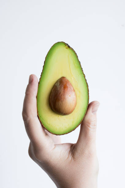 istock Hand holding fresh half avocado with seed on white background 2206354091