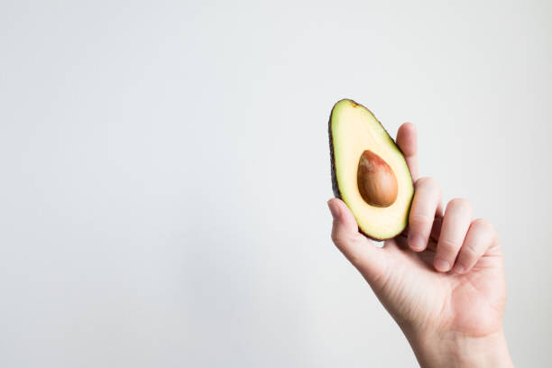 istock Hand holding avocado half against minimalist white background 2206354249