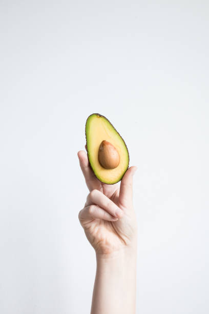 istock Hand holding fresh cut avocado against minimalist white background 2206354472