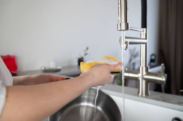 Hands are meticulously washing a pot under a sleek, modern kitchen faucet design A person washes a pot with soap under a sleek kitchen faucet, highlighting cleanliness and modern kitchen design. water sanitation worker washing faucet stock pictures, royalty-free photos & images