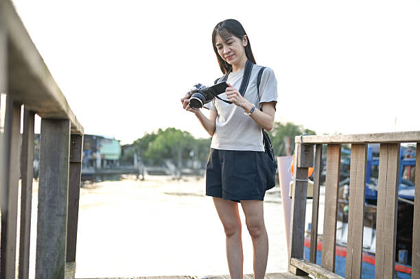 As the sun sets over the fishing village, she stands on the wooden dock, checking the photos on her camera with a satisfied smile
