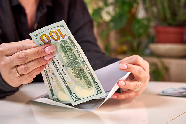 istock A woman puts a stack of dollar bills in an envelope 2206383638