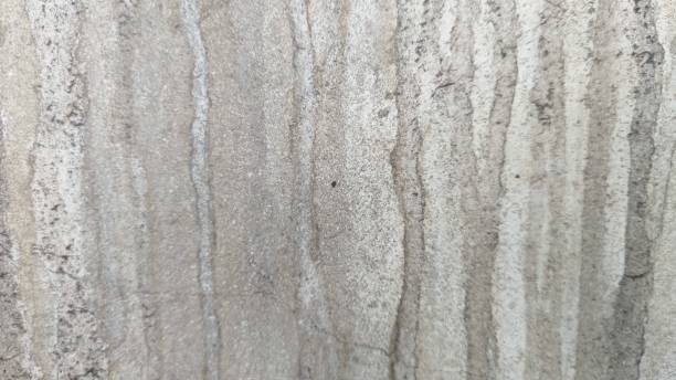 istock The raw grey concrete wall has traces of running water creating vertical lines in various colours of dark grey, light grey, cream and brown. 2206383947