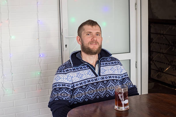 Cheerful redhaired young businessman leaning on the bar counter with a glass of draft beer