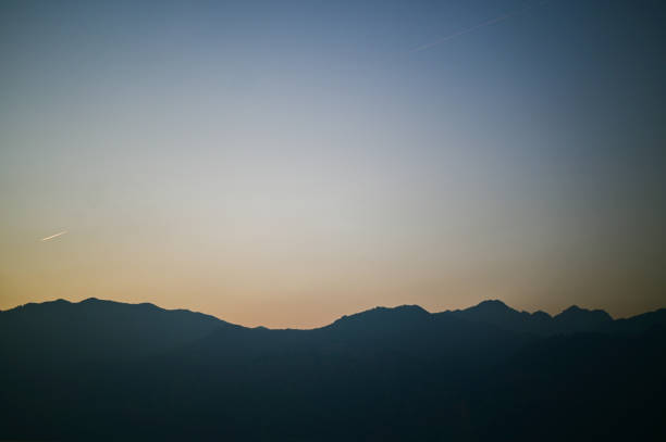 Airplane flying over mountain silhouette at sunset, creating a beautiful contrast between the warm colors of the sky and the dark outline of the mountains