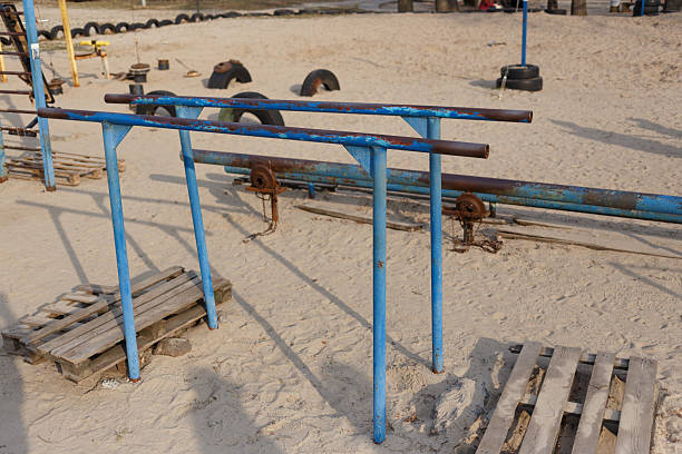 Outdoor exercise equipment at a public calisthenics park on a sunny day, with blue parallel bars and pull-up bars on a sandy surface.
