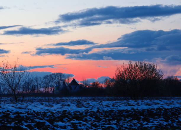 Dark clouds create a dramatic contrast with the bright sky, while the silhouettes of trees and a building on the horizon add depth and mystery.