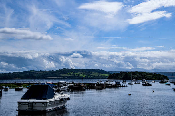Boats sit waiting for their owners on a loch in Scotland on a perfect day with fluffy clouds.