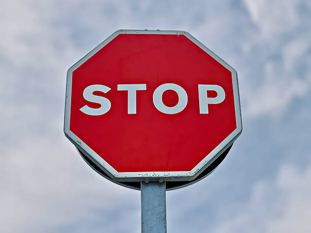 istock Red stop sign with white letters on metal pole against cloudy sky 2206409405
