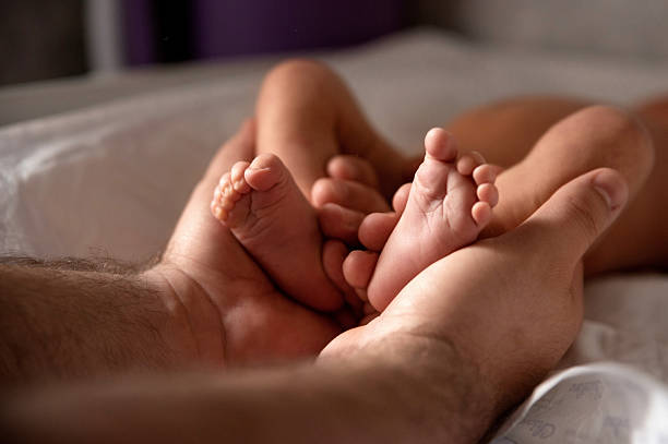 Father holding newborn baby's legs on soft bed