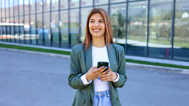 istock Smiling businesswoman using smartphone in front of modern office building 2206426378