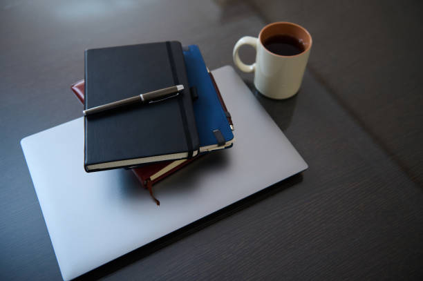 An organized arrangement of a laptop, stacked notebooks, a pen, and a steaming coffee, conveying productivity and inspiration.