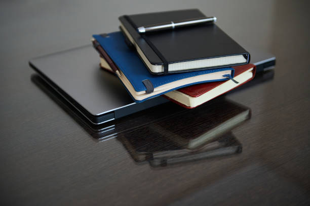 Stacked Notebooks and Laptop on a Reflective Wooden Desk