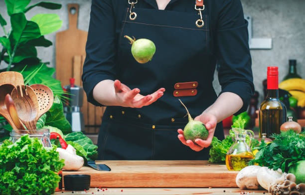 istock Chef throws up green radish in hands. Cozy kitchen with wooden table, kitchenware, vegetables, herbs and ingredients for cooking. Healthy vegan eating, culinary, recipes, food blogging 2206458171