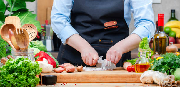 istock Home cook cuts shallots onion with knife in cozy kitchen with wooden table, kitchenware, vegetables, herbs and ingredients for cooking. Healthy vegan food, culinary, recipes, food blogging 2206458192