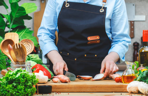 istock Chef cuts shallots onion in cozy kitchen with wooden table, kitchenware, vegetables, herbs and ingredients for cooking. Healthy vegan food, culinary, recipes, food blogging 2206458198