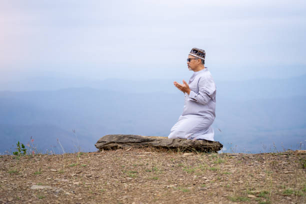 An elderly Muslim man praying on a mountain.