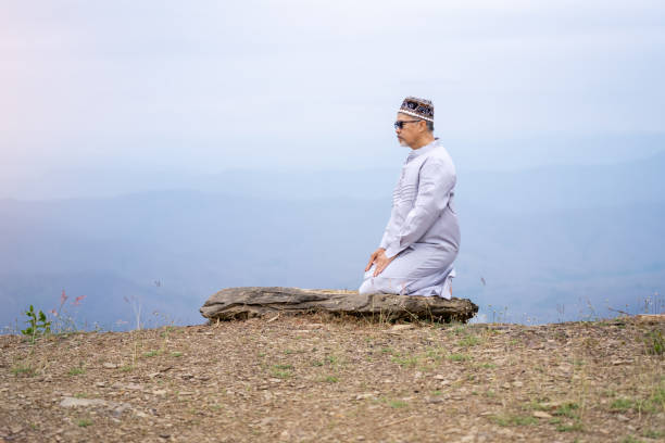 An elderly Muslim man praying on a mountain.